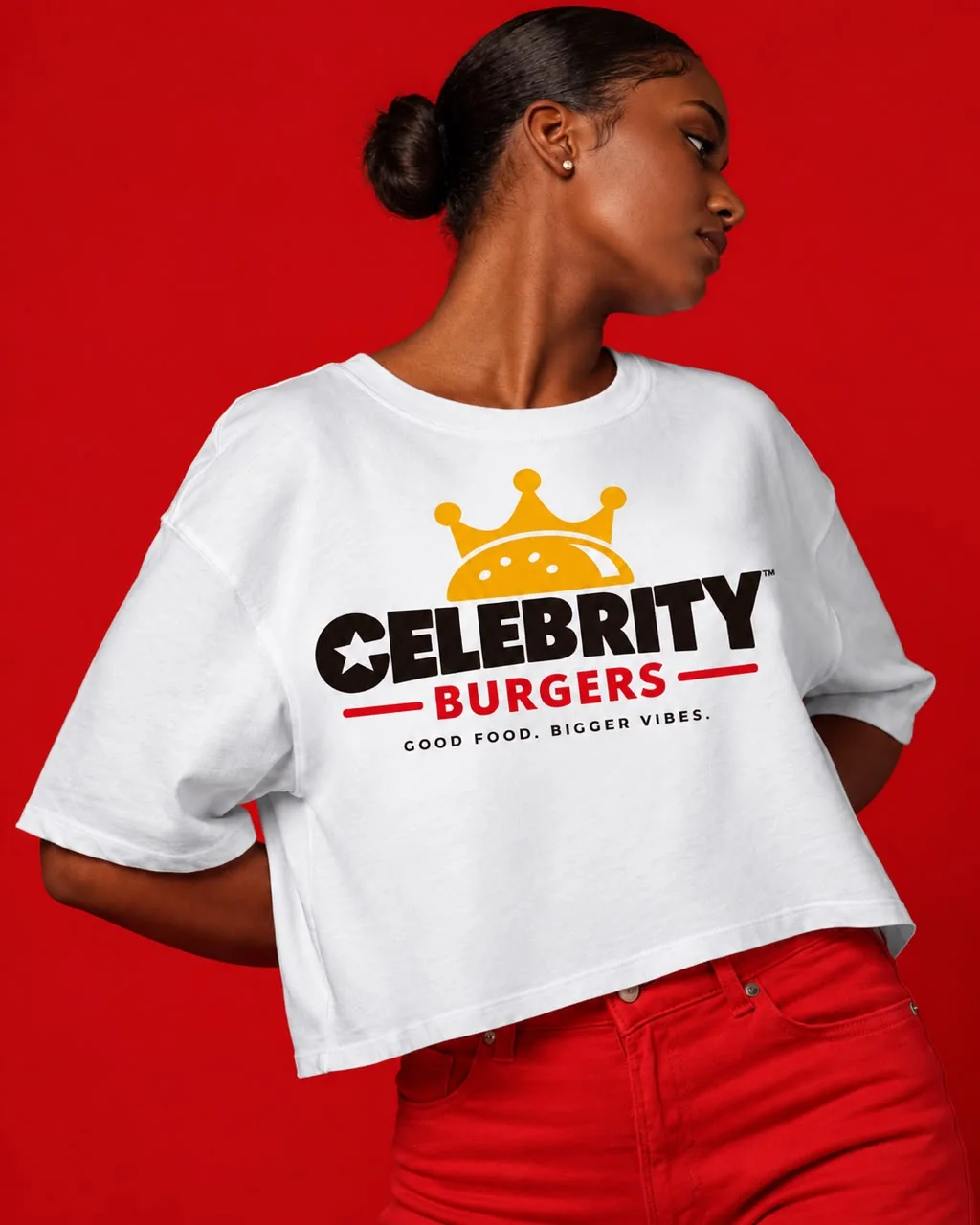 A woman in a white cropped Celebrity Burgers t-shirt against a red backdrop