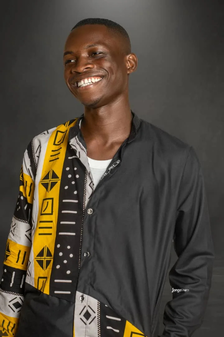 Tumbu John smiling in a black shirt with a yellow and black patterned sleeve